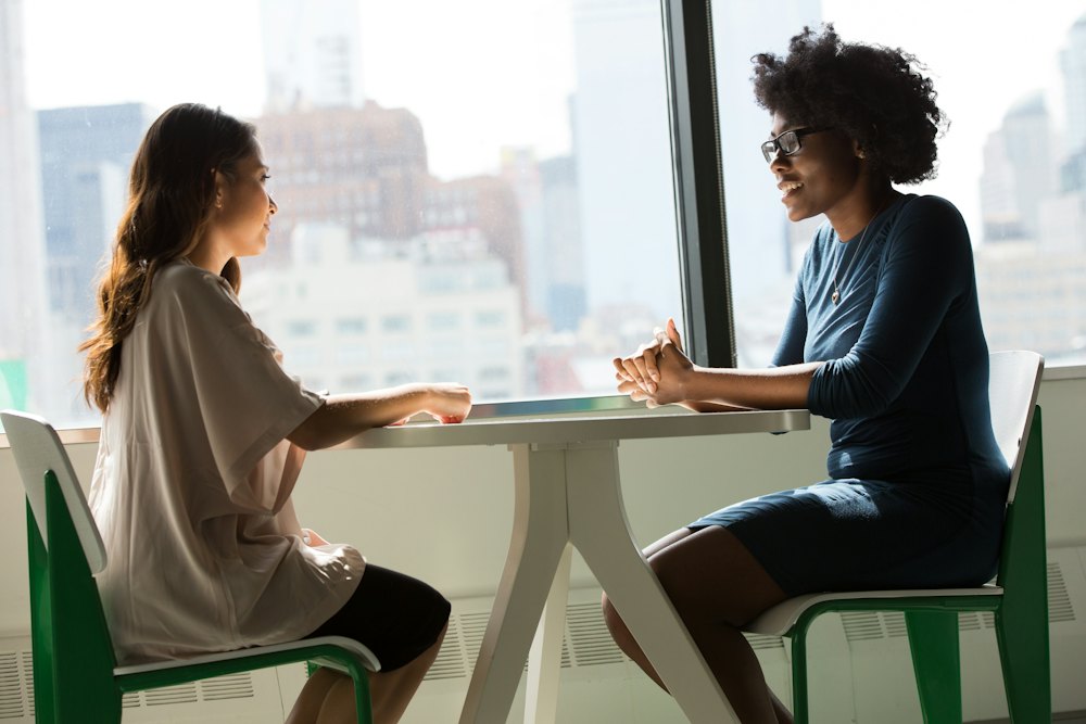 Two people talking across a table by the window