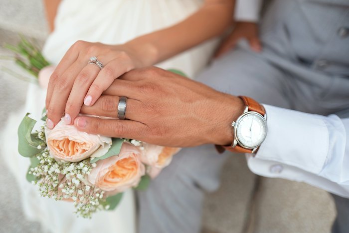 Couple holding hands with wedding rings over a bouquet