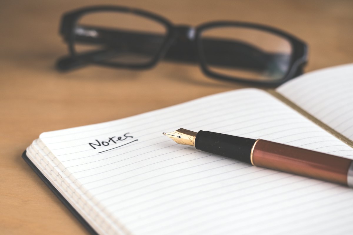 A desk with a notebook, pen and laptop