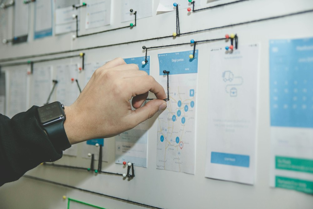 Hand pointing at wireframe sketches pinned to a wall