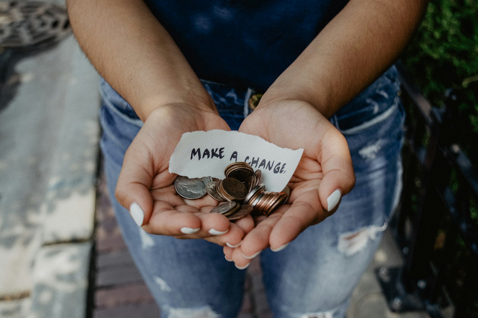 Hands cupped together holding coins and a handwritten note reading Make a change