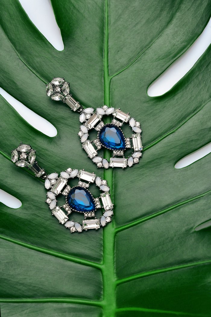 Sapphire and diamond drop earrings on a green leaf