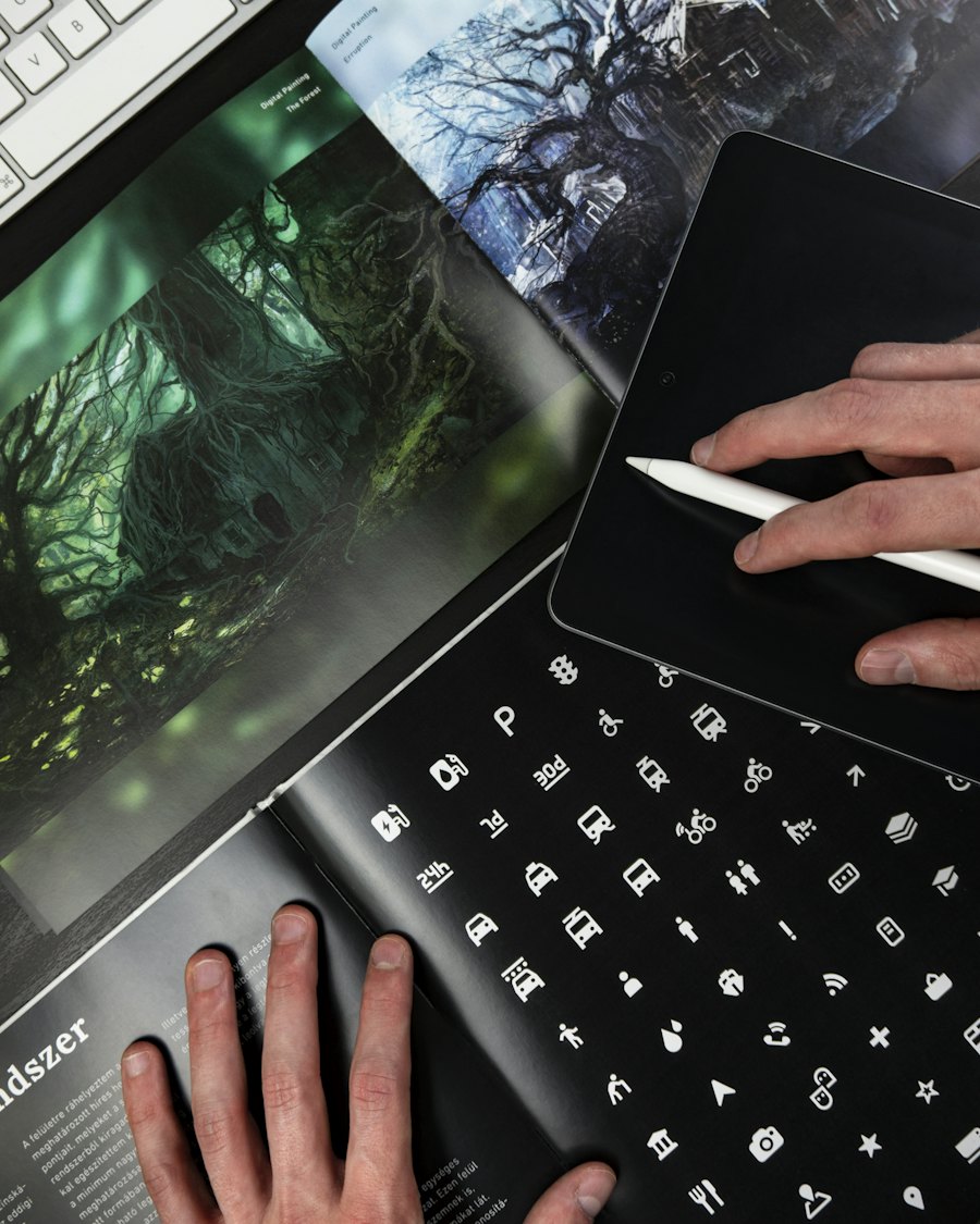A laptop showing a design project next to a notebook