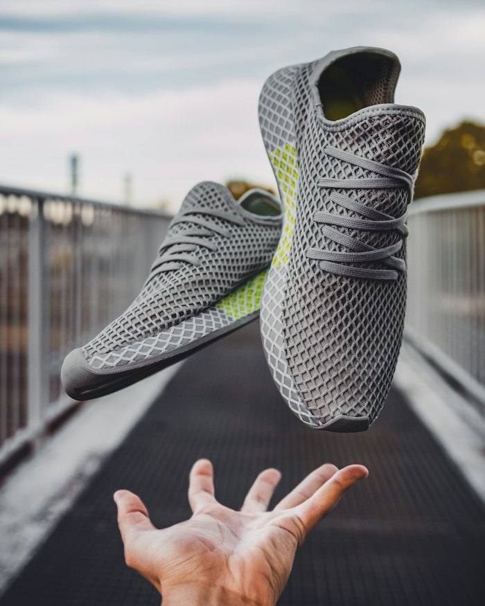 Grey knit sneaker tossed in the air above a hand