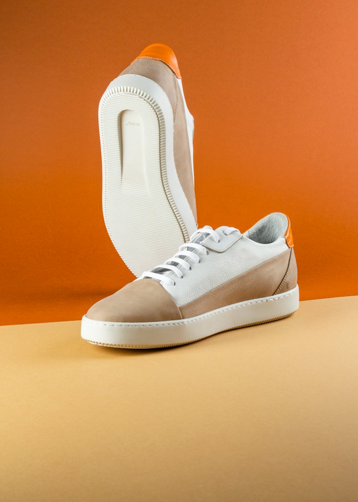 Beige and white low-top sneaker on an orange background