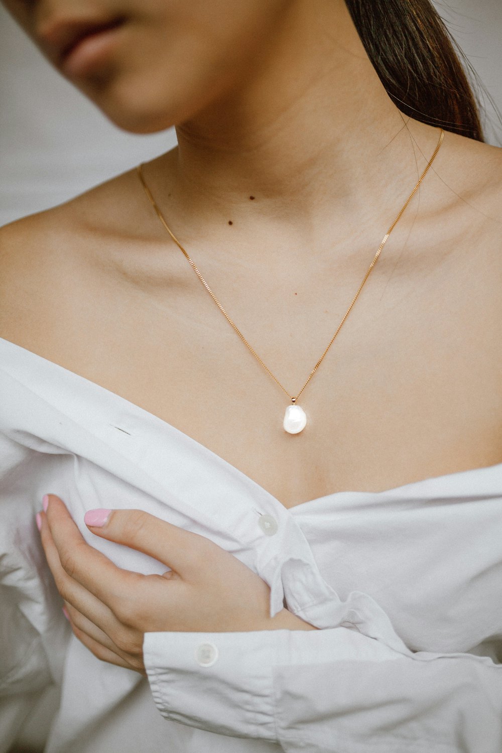 Woman in a white blouse wearing a fine pendant necklace
