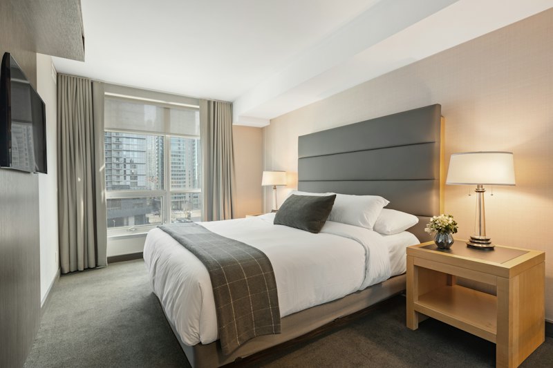 Compact hotel room with a made bed and warm bedside lamp